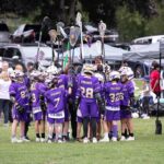 A team of lacrosse players with purple jerserys and sticks in the air.