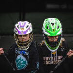 Two lacrosse players in helmets with sticks.