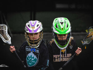 Two lacrosse players in helmets with sticks.