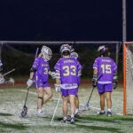 Three lacrosse players in front of a goal.