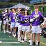 A line of lacrosse players in a line during the national anthem .