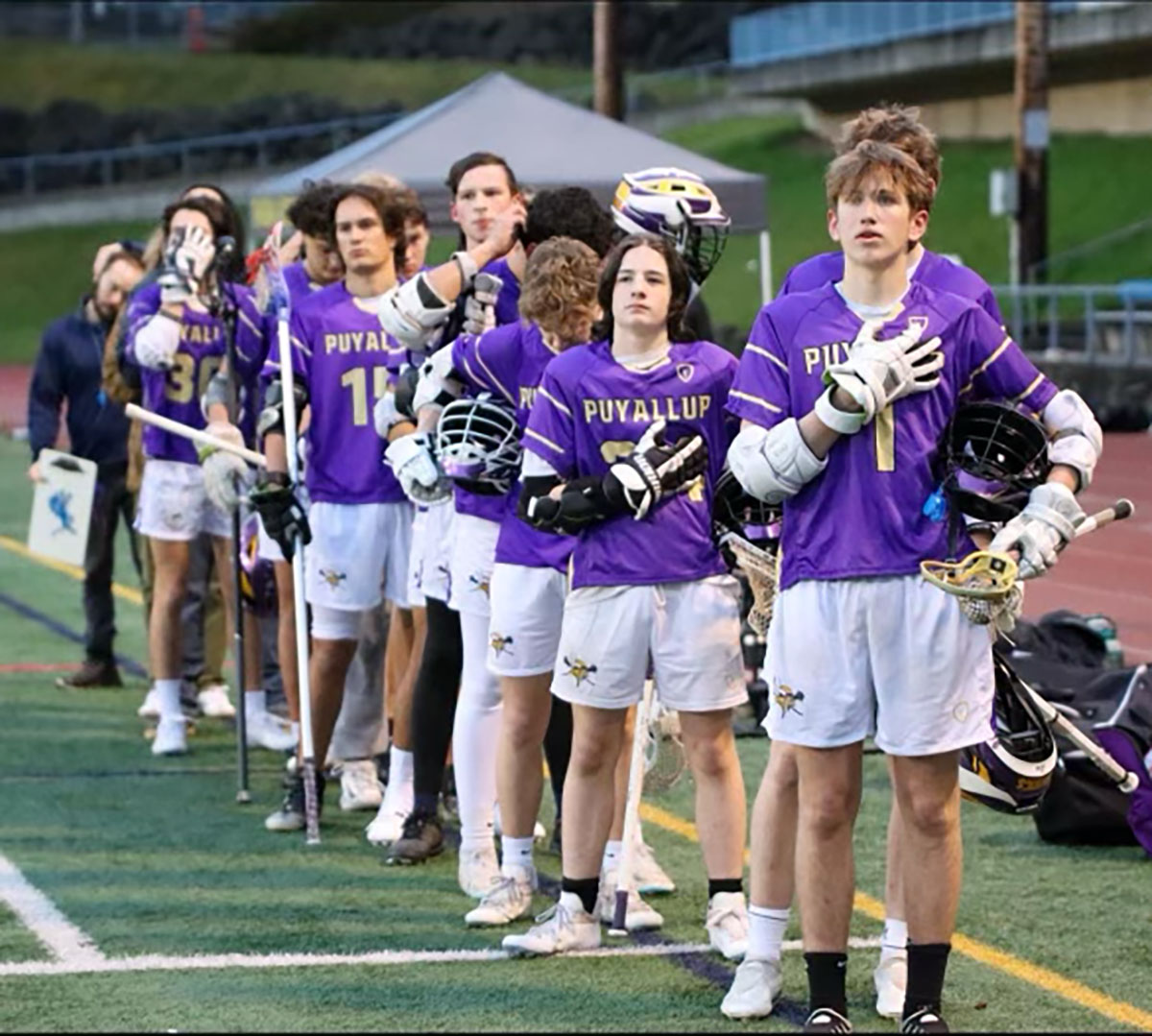 A line of lacrosse players in a line during the national anthem .