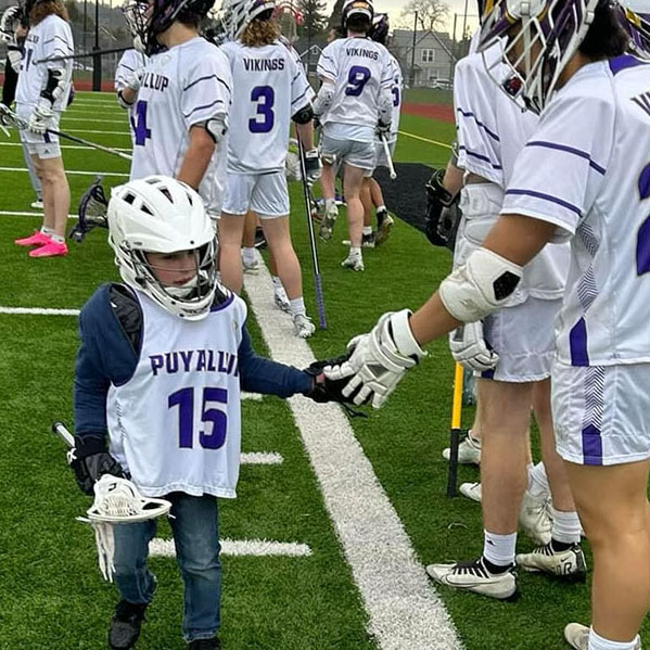 A kindergarten lacrosse player giving a high school player a high five.